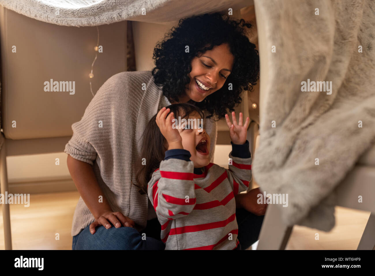 Mutter und ihre kleine Tochter spielen in eine Decke fort Stockfoto