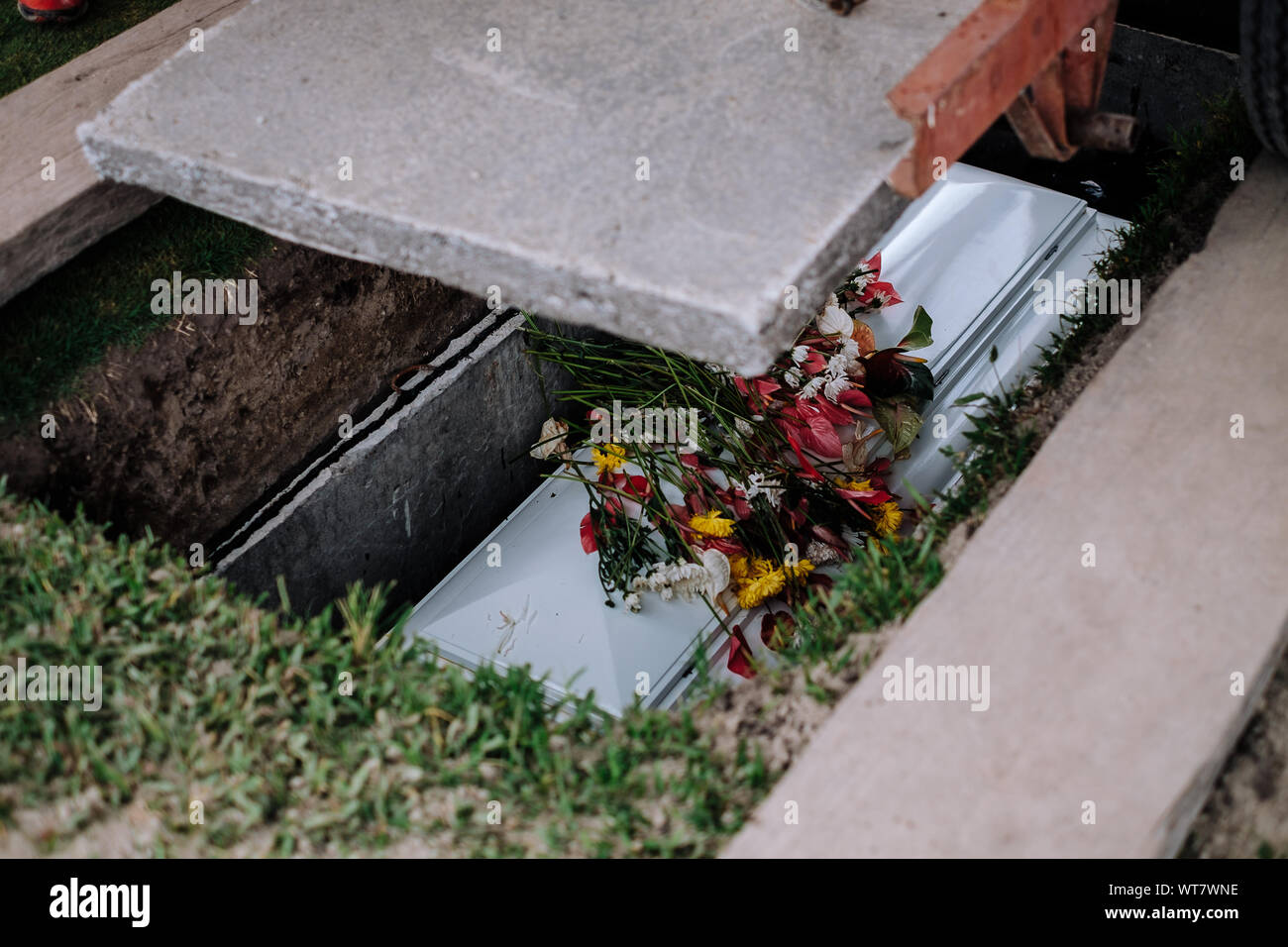 Zement Platte wurde reduziert den Sarg zu decken. Sarg der Toten, mit Blumen von Familie und Bekannten an der Spitze, der Rest auf dem Boden. Stockfoto