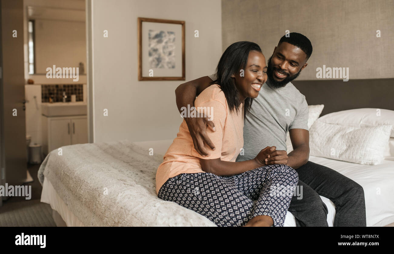 Junge afrikanische amerikanische Paar sitzt auf ihrem Bett und zusammen lachen Stockfoto