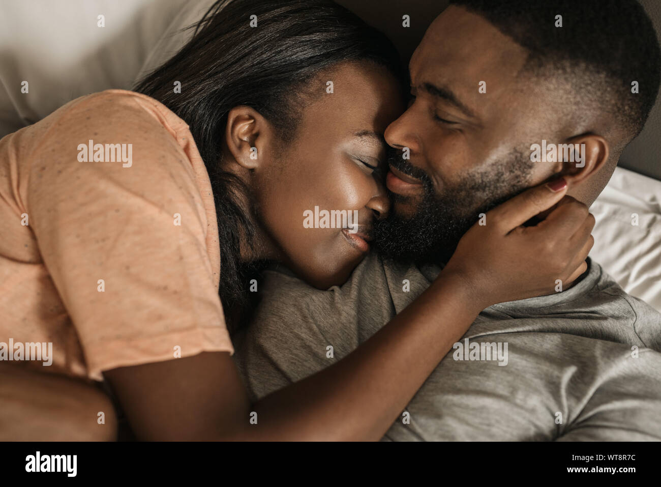Lächelnden jungen afrikanischen amerikanischen Paar umarmen im Bett Stockfoto