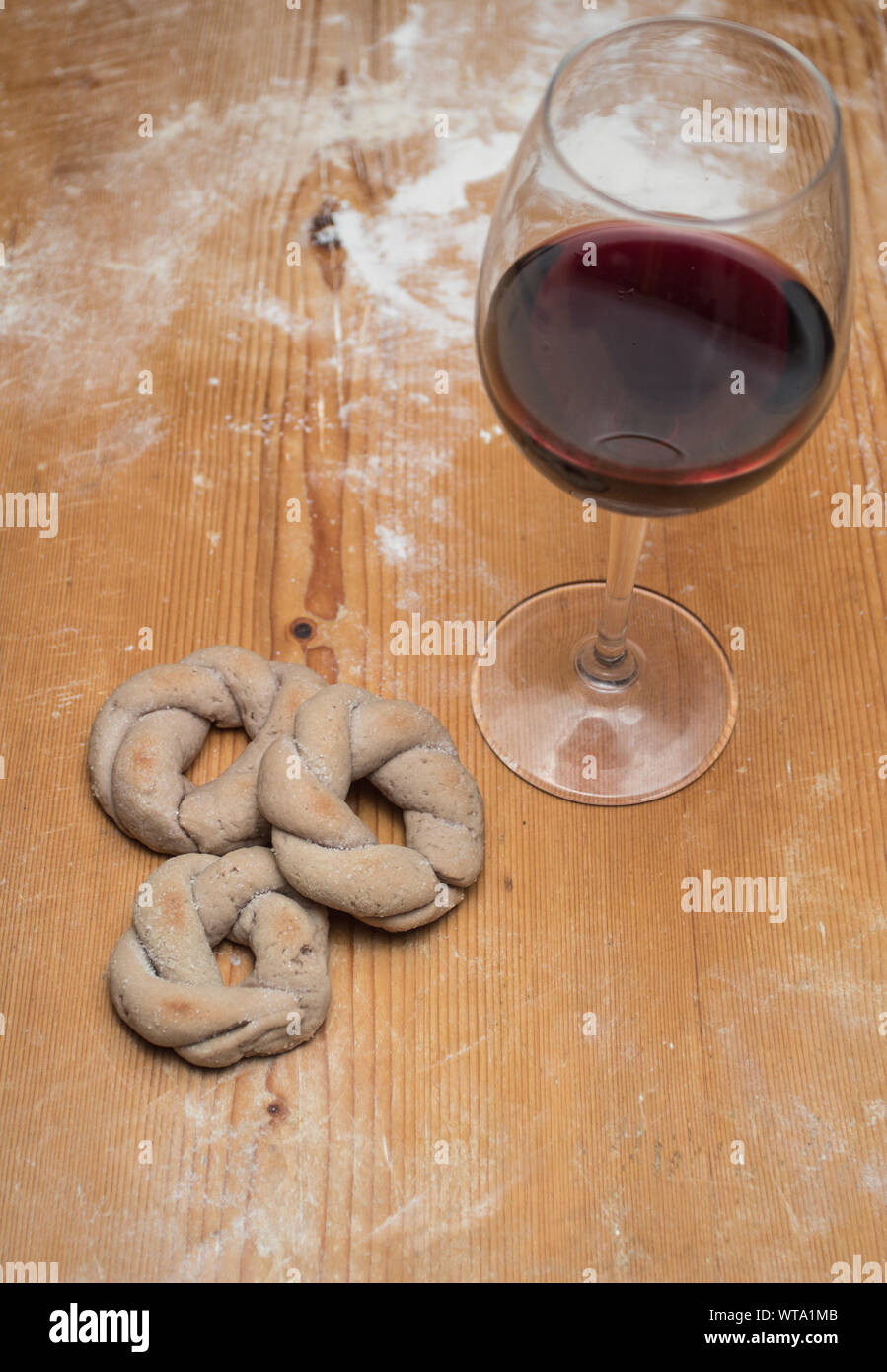 Italienischer Rotwein ciambelline Kekse, gekocht, mit Rotwein Glas auf Holz- Bemehlten tisch Hintergrund. Vertikale Ausrichtung. Stockfoto