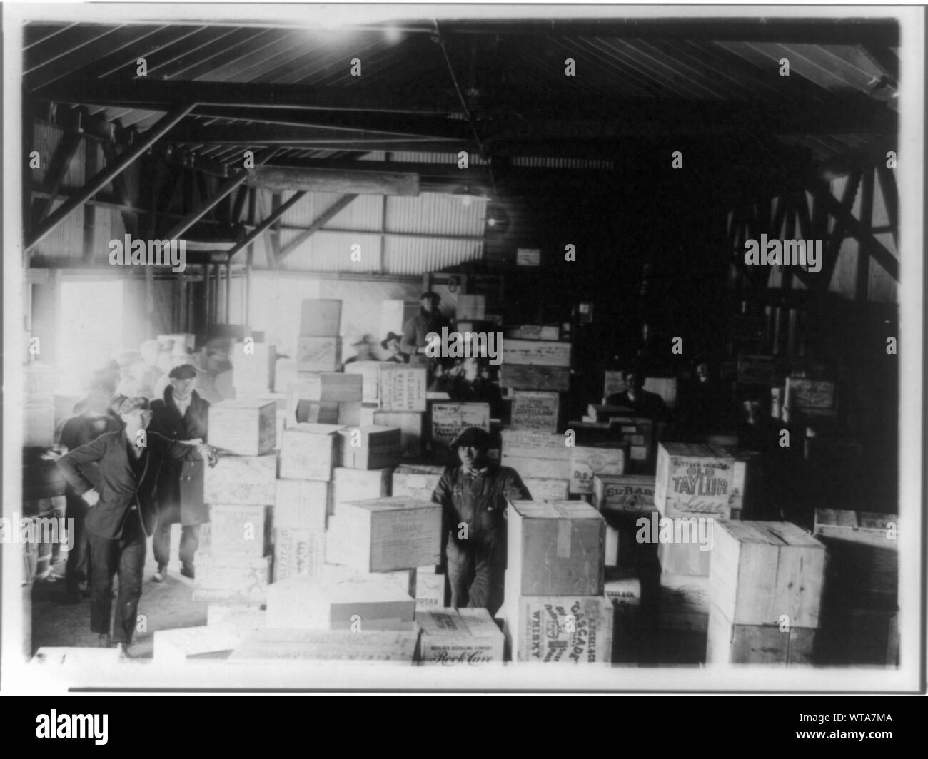 Stehende Männer im Lager mit Fällen beschlagnahmt (?) Schnaps Stockfoto