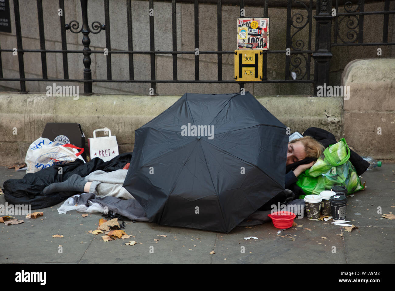 Obdachlosen schläft auf einer Straße im Zentrum von London in der Nähe von Trafalgar Square geschützt etwas durch einen Regenschirm gegen den Regen. Stockfoto