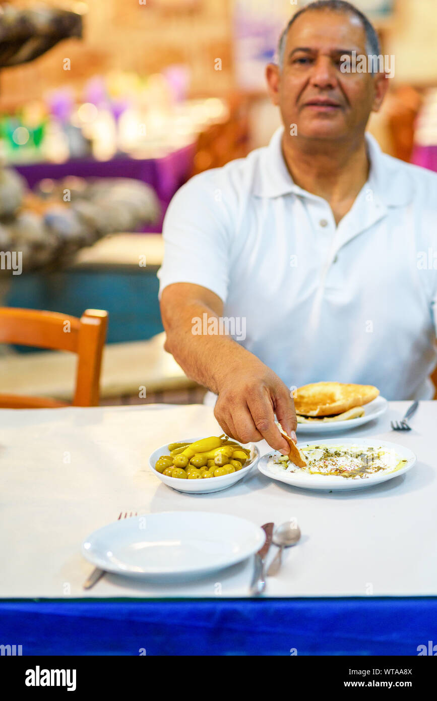 Älterer Mann labneh mit pita Brot essen. Labneh - Weichkäse, ähnlich in der Textur zu Frischkäse, aus belasteten Joghurt gemacht und sehr beliebt in nahöstlichen Küche. Selektiver Fokus auf Hand und Essen. Stockfoto