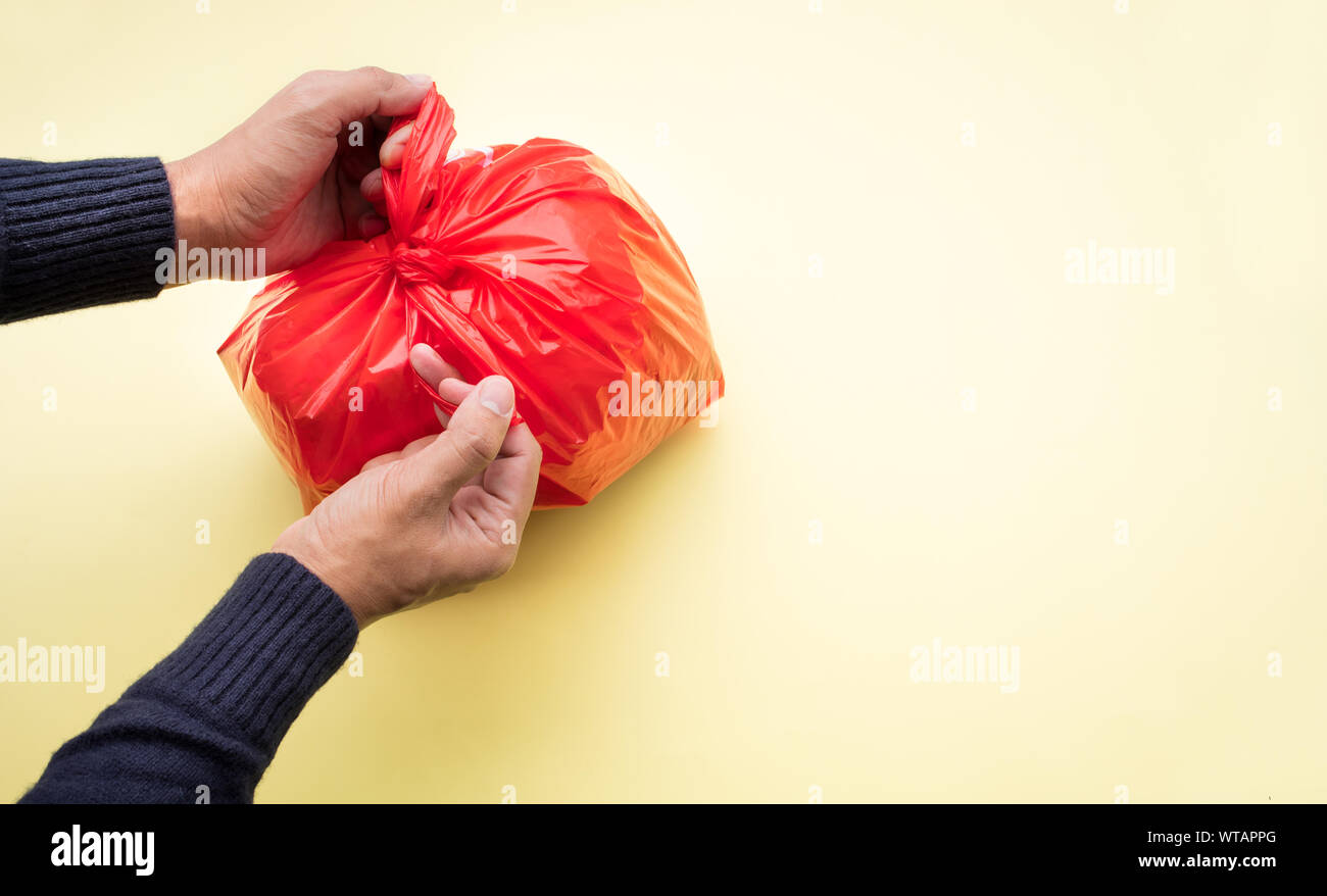 Männliche hand Verpackung Lebensmittel Papierkorb mit rotem Kunststoff Beutel auf Farbe Hintergrund. Recycling und Umwelt Konzepte Ideen Stockfoto