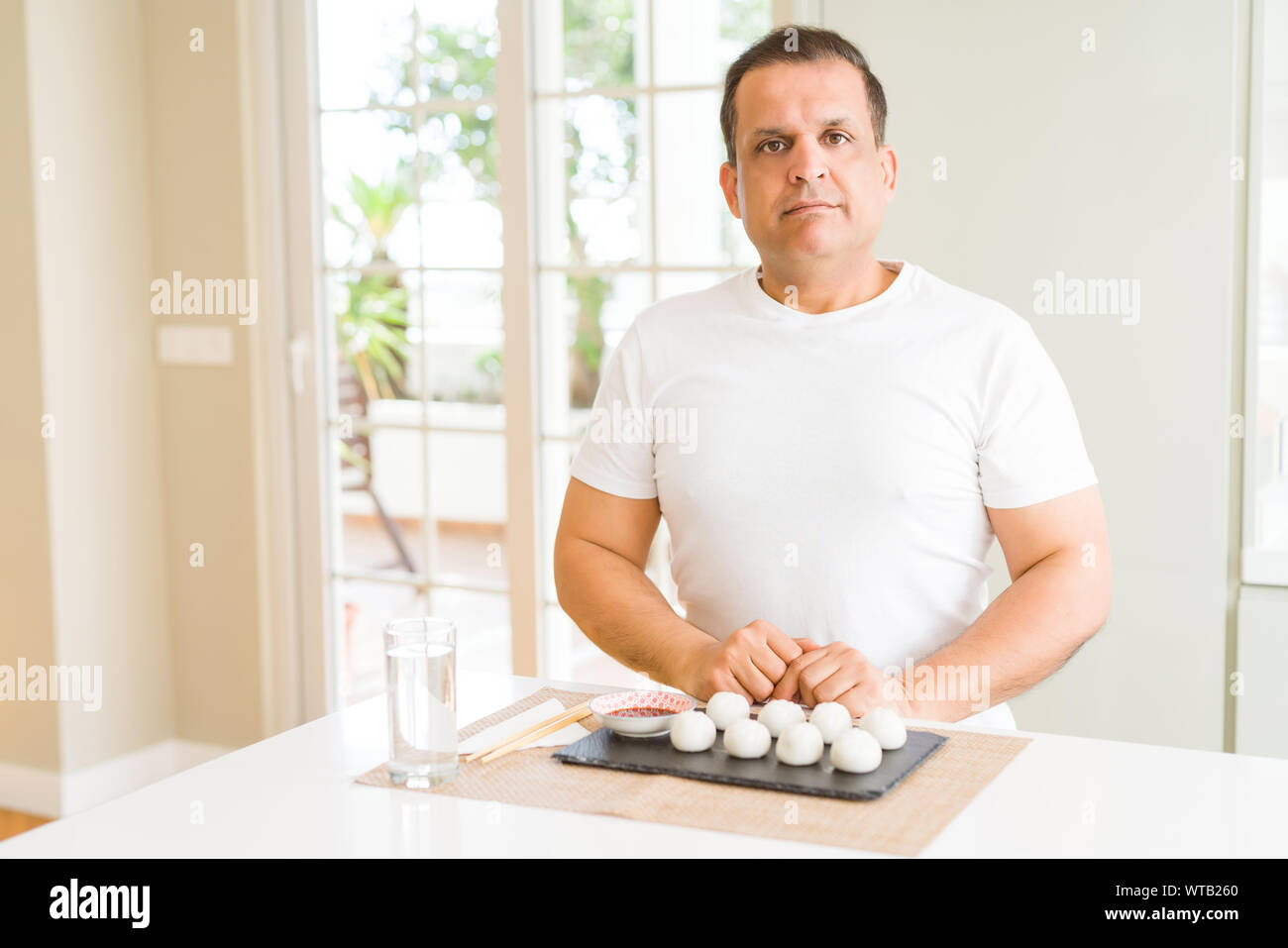 Mittleres Alter mann Essen asiatische Knödel zu Hause mit ernsten Gesichtsausdruck. Einfache und natürliche in die Kamera schaut. Stockfoto