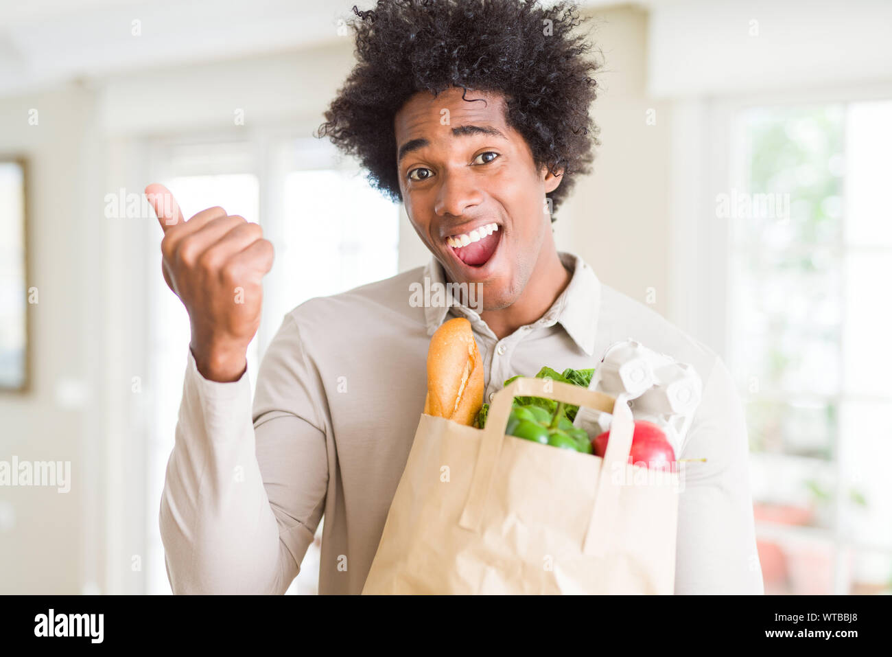 Afrikanische amerikanische Mann hält Lebensmittel Beutel mit frischem Gemüse zu Hause schreien stolz und feiern Sieg und Erfolg sehr aufgeregt, jubelnde em Stockfoto