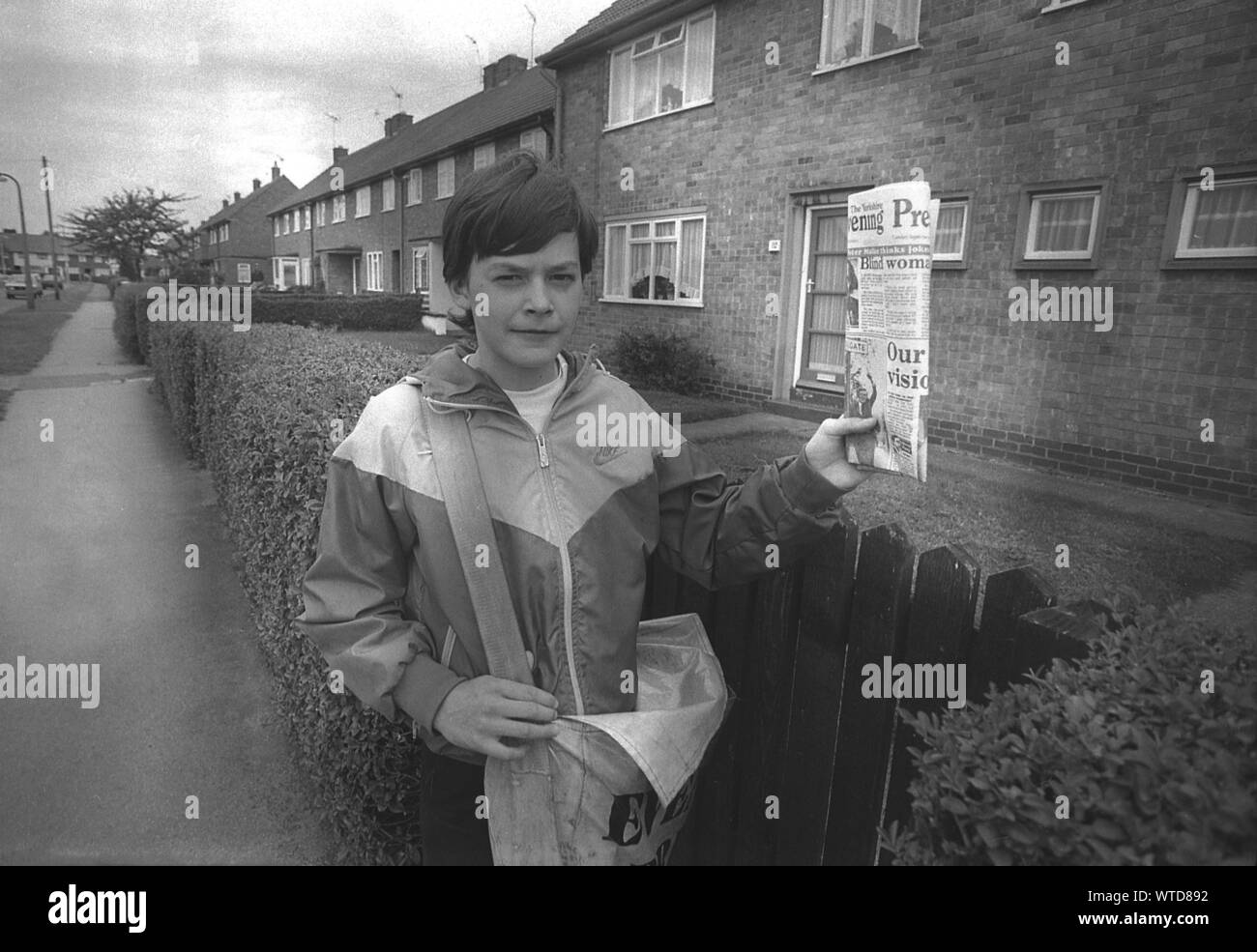 1980 s, historischen, nach der Schule, ein paperboy mit Ranzen, seine Nachmittag oder frühen Abend Papier runde Tun auf einer Wohnsiedlung, England, UK. Oft erster Job eines jungen Menschen, es gab Ihnen Ihre erste Erfahrung mit der Arbeit und ein kleines Einkommen, aber die verlieren viele Abend gedruckte Zeitungen hat Zahlen aus früheren Jahrzehnten rapide abnehmen. Stockfoto