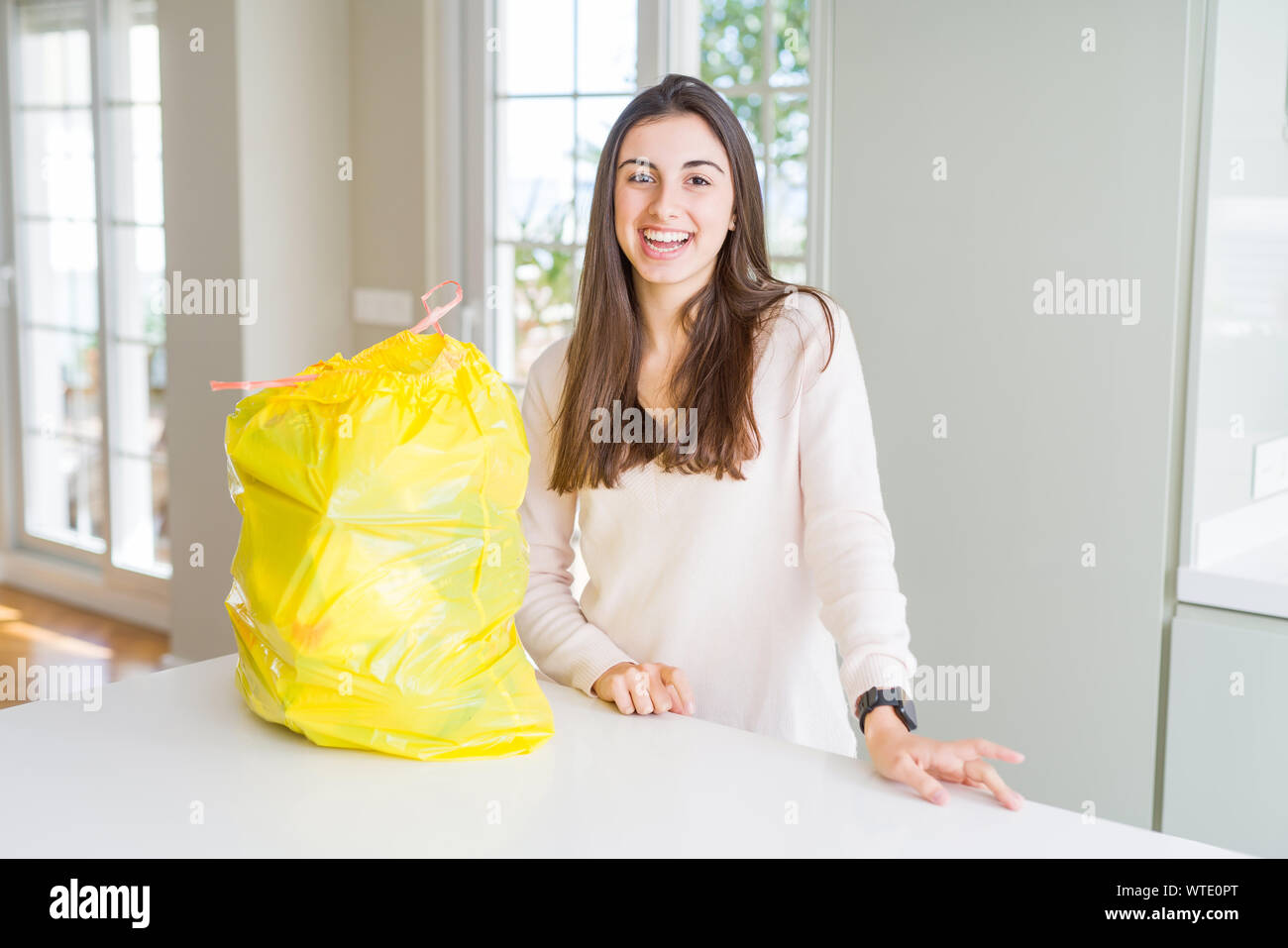 Schöne junge Frau, die den Müll aus dem Müll container mit einem glücklichen und kühlen Lächeln auf dem Gesicht. Glückliche Person. Stockfoto