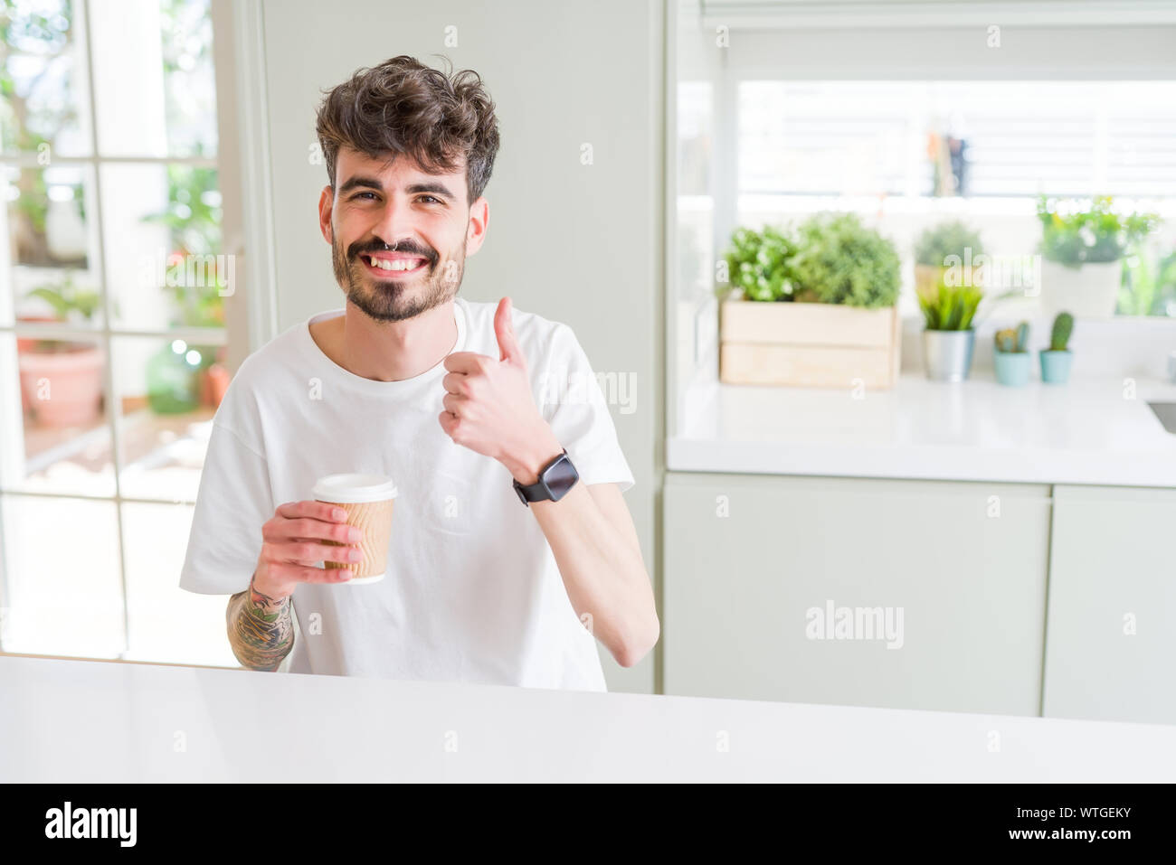 Junger Mann, trinken einen Kaffee in einer Tasse am mit einem großen Lächeln tun ok
