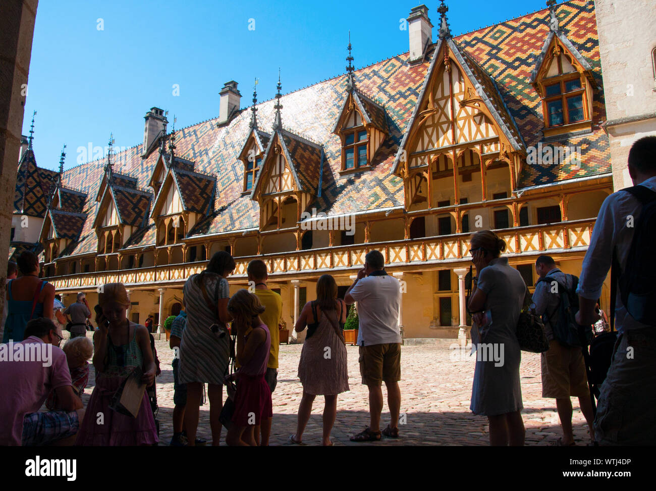 Touristen im Schatten auf dem Hof des Hospices de Beaune mit seinen wunderschön gestalteten Dach. Beaune, Burgund, Frankreich. Stockfoto
