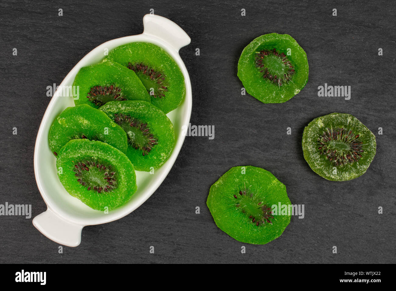 Gruppe der acht Scheiben süß grün kandierte Kiwis in weiße, ovale Keramik Schüssel flatlay am grauen Stein Stockfoto