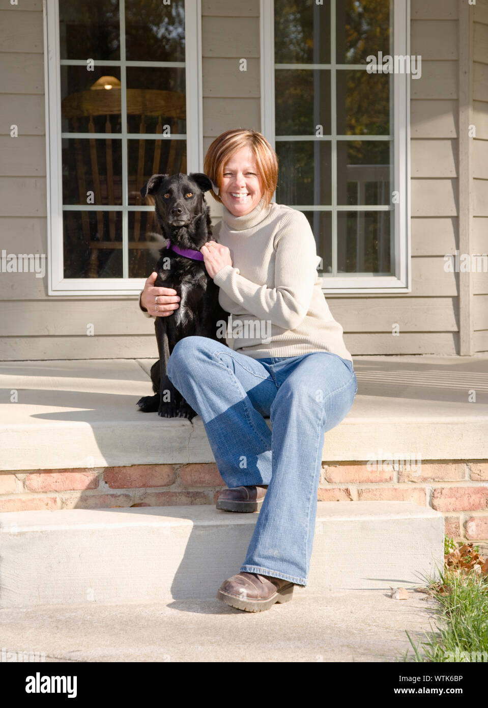 Portrait von lächelnden Frau sitzt auf der Veranda mit Hund Stockfoto