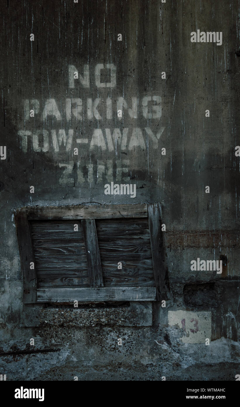 Ein dunkles, grungiges Bild, das eine alte Holzpalette zeigt, die auf ihrem Ende unter der Aufschrift „No Parking Tow-Away Zone“ steht. Stockfoto
