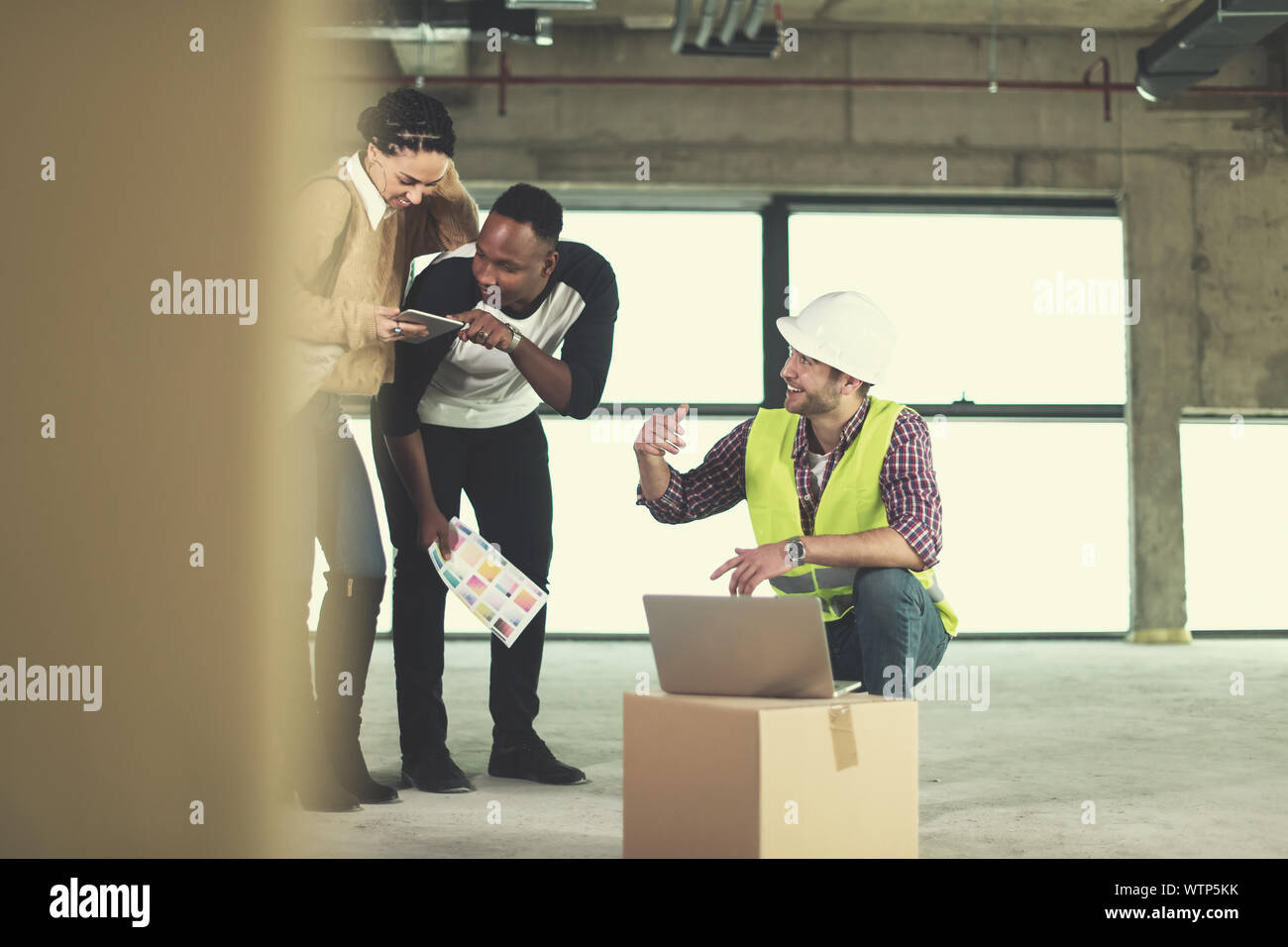 Architekt Ingenieur mit Laptop Computer und zeigt Haus Design plant, eine junge, multiethnische Paar an der Baustelle Stockfoto