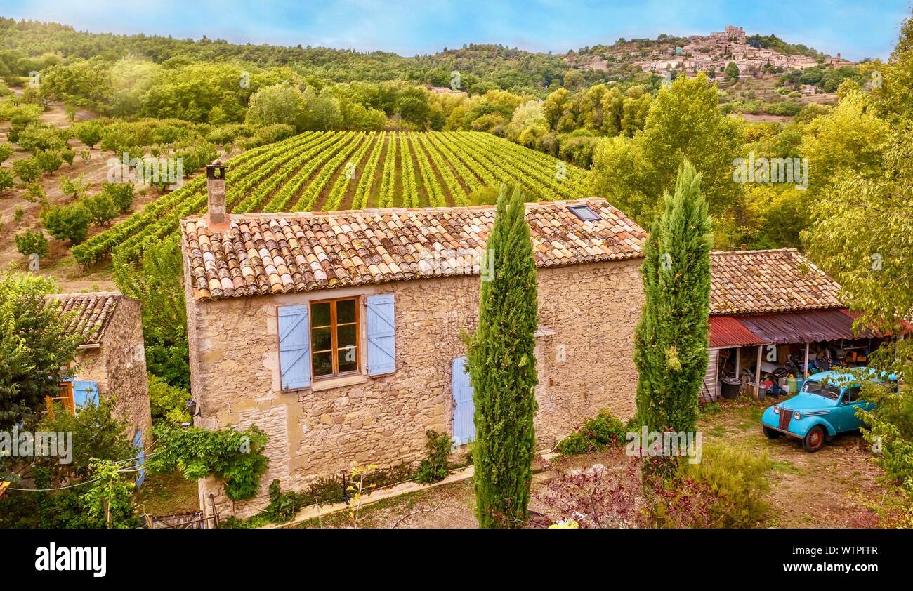 Hohe Betrachtungswinkel von einer Straße von einem traditionellen alten Bauernhof aus Stein Haus und malerischen Traube Weinberg, mit symmetrischen Reihen von Reben in der Provence, Frankreich. Stockfoto