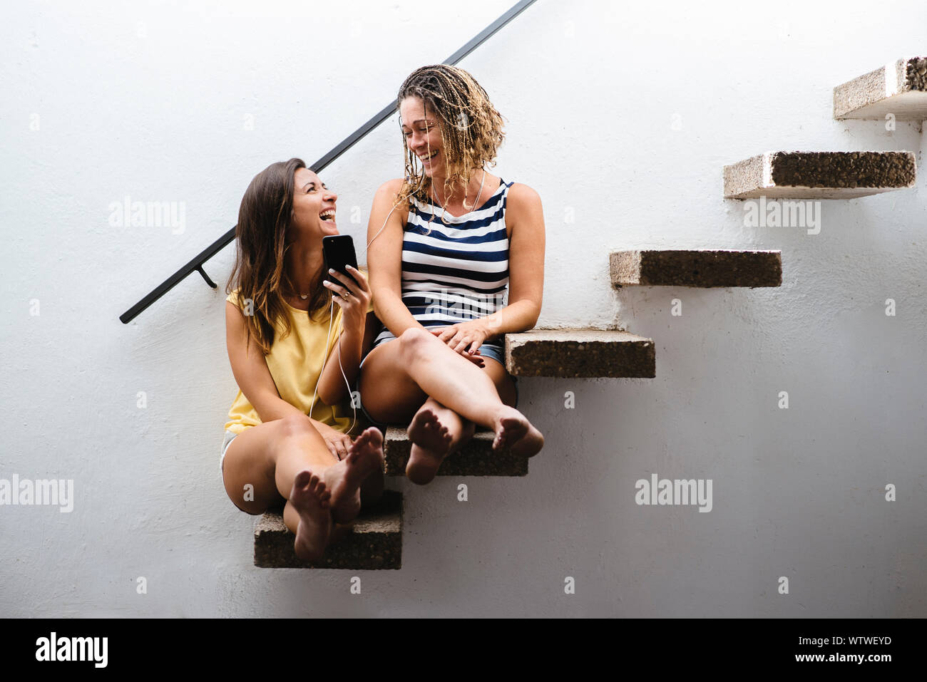 Zwei Frauen sitzen auf der Treppe zu lachen, während Sie Musik hören. Stockfoto