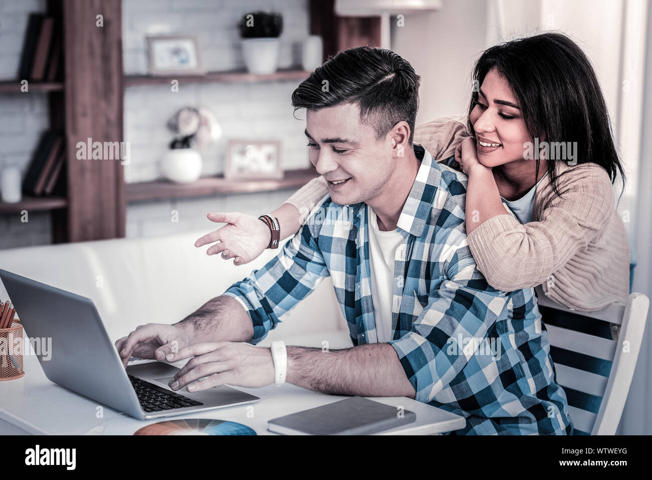 Mann mit modischen Haarschnitt arbeiten mit Laptop, während seine Freundin schiefen Stockfoto