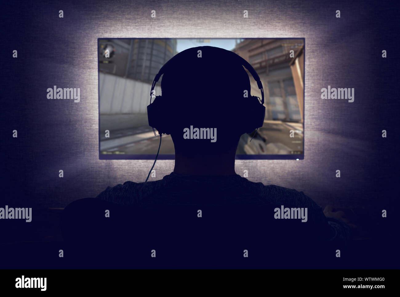 Gamer in der Kopfhörer sitzt vor einem leeren Monitor im dunklen Zimmer Stockfoto