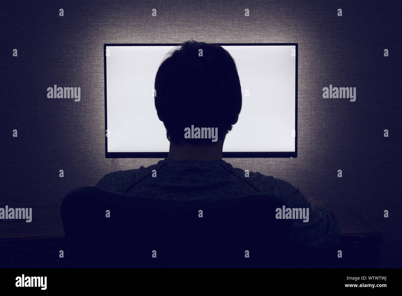 Mann sitzt vor einem leeren Monitor im dunklen Zimmer Stockfoto