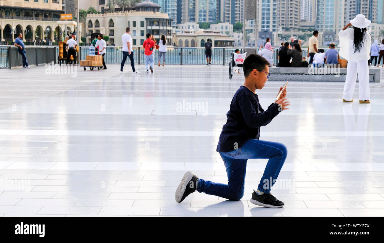 Dubai, Vereinigte Arabische Emirate - 31. Oktober, 2018: Touristische versammeln sich auf der Dubai Mall entfernt. Ein junger asiatischer Boy kniet ein Bild zu machen. Stockfoto