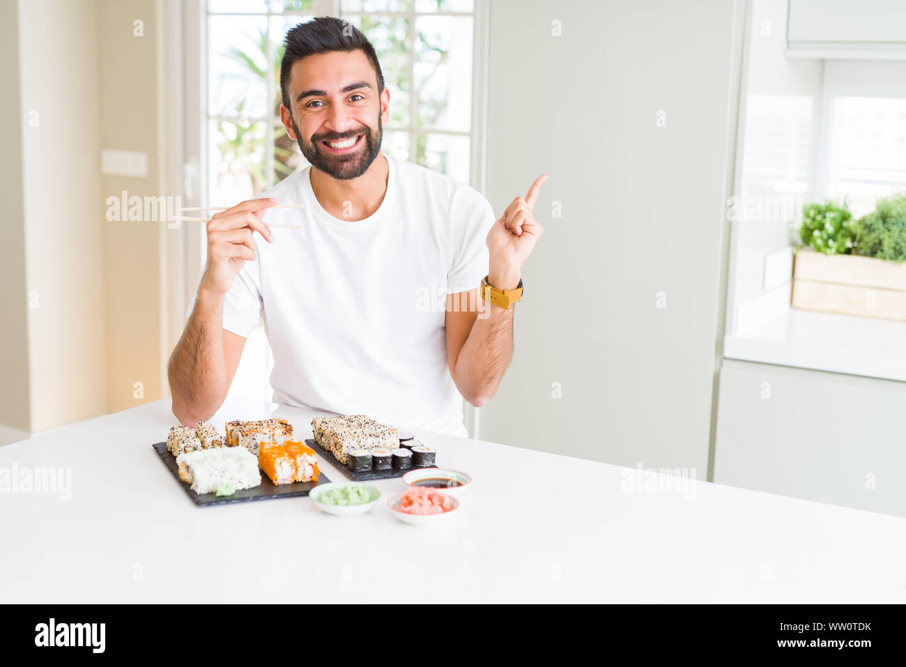 Stattliche Hispanic Mann essen asiatische Sushi mit Stäbchen sehr zufrieden zeigt mit Finger- und an der Seite Stockfoto