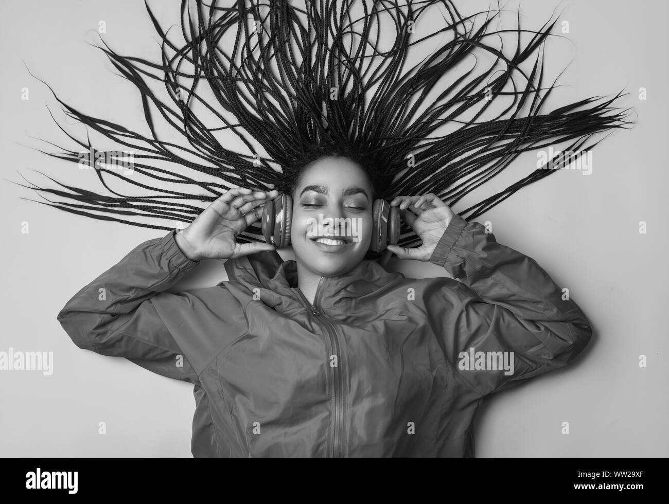 Portrait von wunderschönen afrikanischen brunette teenage Mädchen mit Dreadlocks tragen einen roten windbreaker Musik hören über kabellose Kopfhörer isoliert auf Vivi Stockfoto