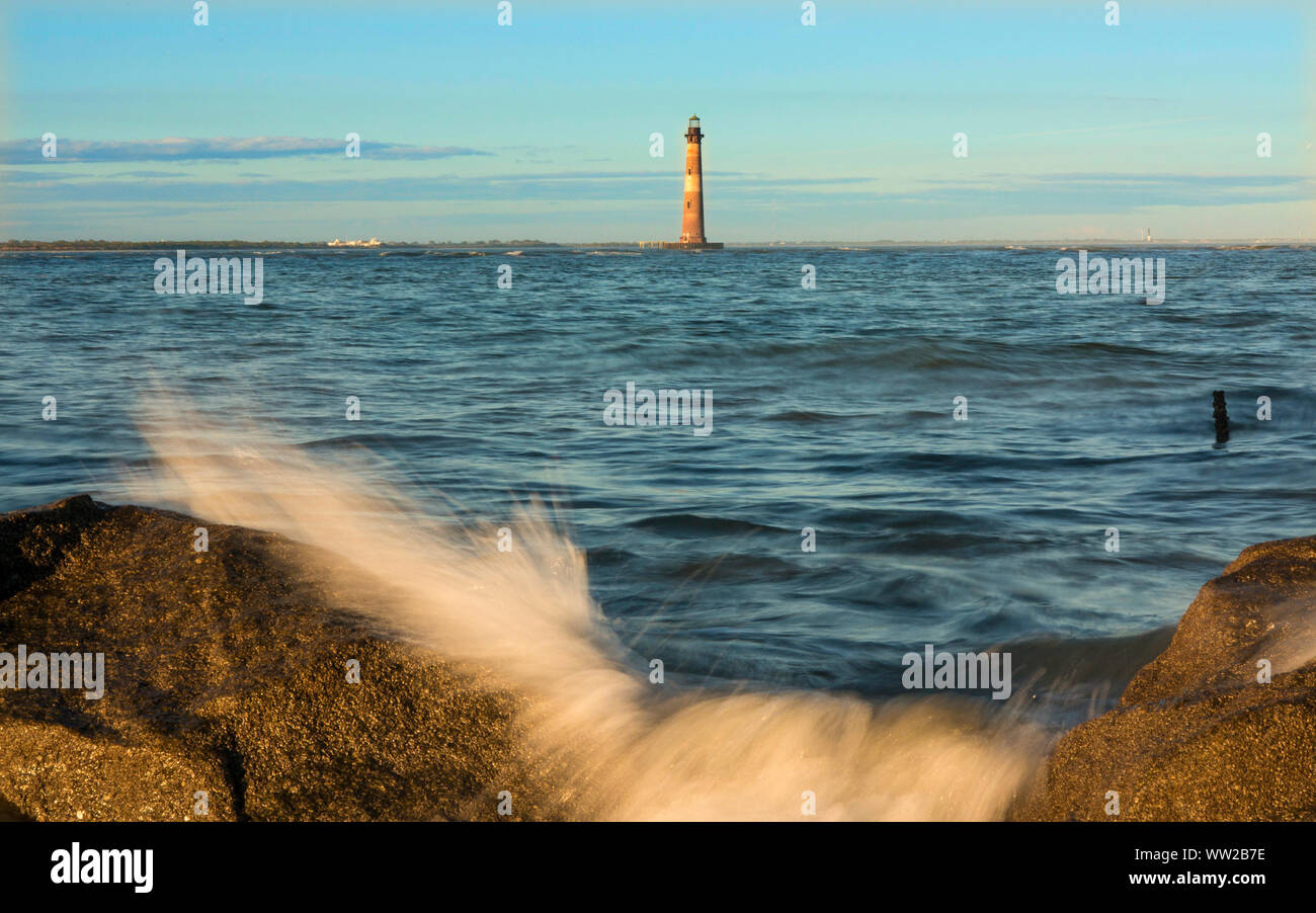 Leuchtturm im Meer mit Wellen, die über Felsen Stockfoto