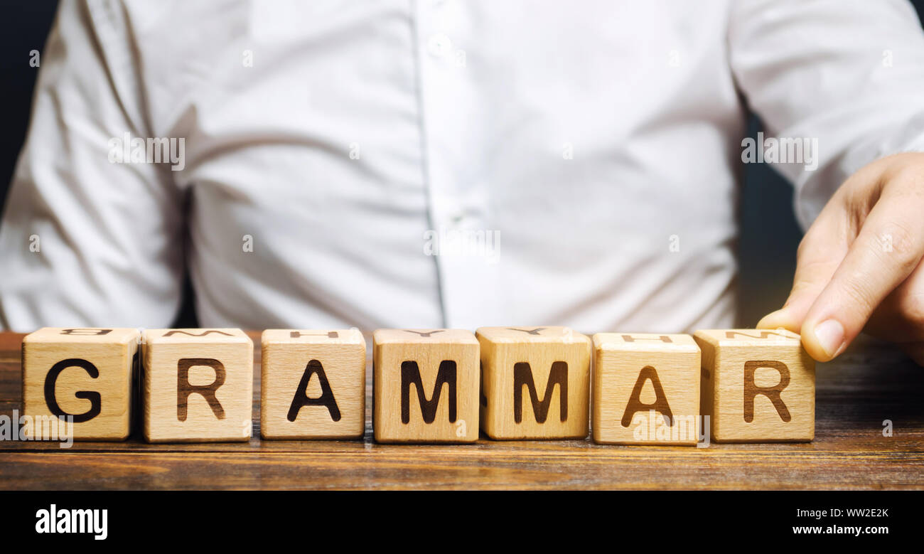 Ein Mann legt Holzblöcke mit dem Wort Grammatik. Satz von strukturellen Regeln für die Zusammensetzung von Klauseln, Phrasen und Wörter, die in einer natürlichen Sprache. Stockfoto