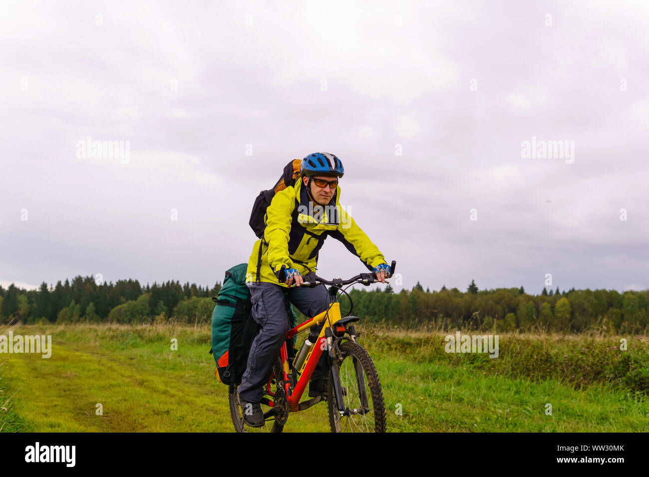 Männliche bikepacker reitet auf einem Feldweg durch ein Feld an einem bewölkten Herbst Tag Stockfoto