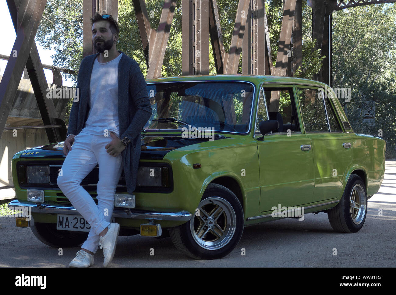 Junger Mann in weißen Jeans lehnte stolz gegen eine schön Restaurierte Vintage 70er JAHRE SITZ 124 oder FIAT Auto in der Sonne in Spanien Stockfoto