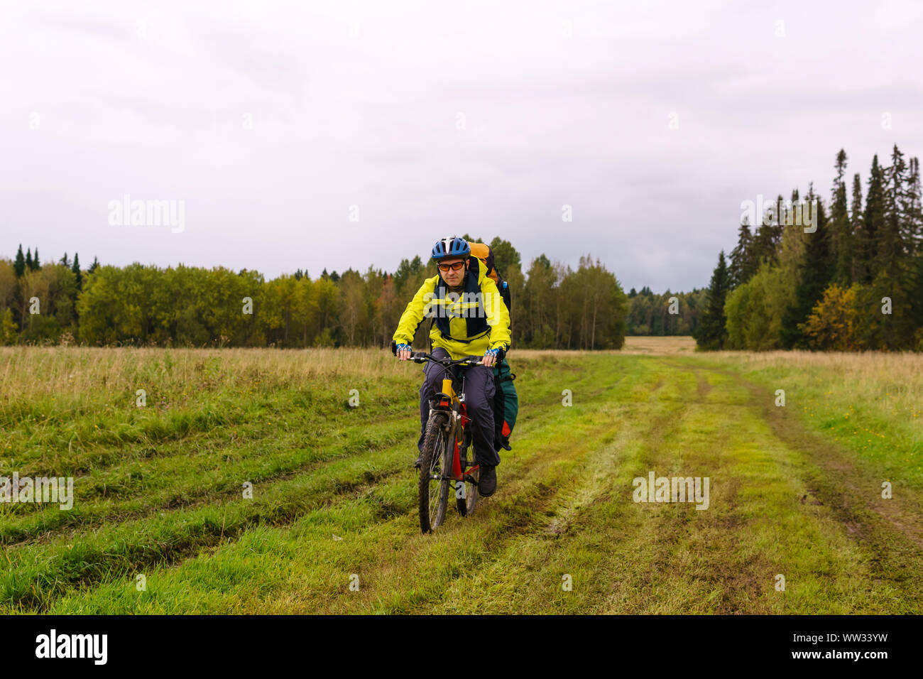 Männliche Radfahrer Wanderer fährt auf einer Schotterstraße durch ein Feld an einem bewölkten Herbst Tag Stockfoto