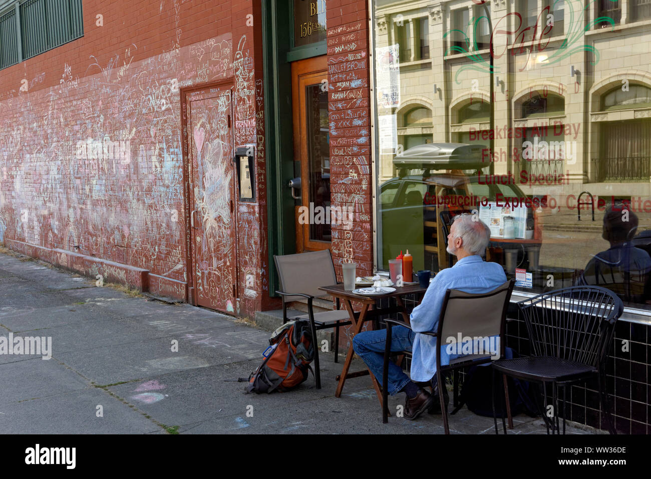 Ältere Menschen allein an einem Tisch draußen ein Restaurant Cafe in der Mount Pleasant Viertel von Vancouver, BC, Kanada sitzen Stockfoto