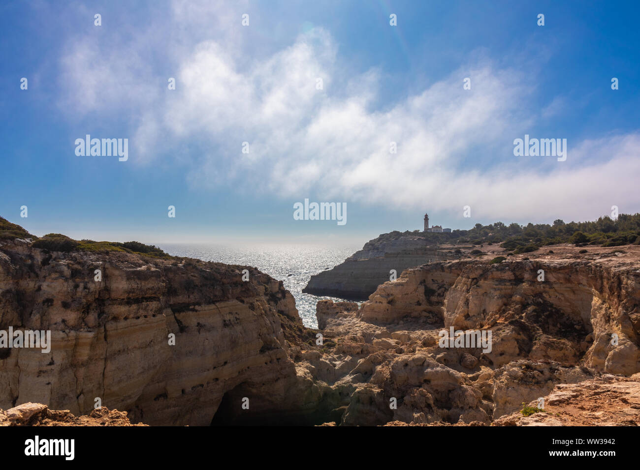Felsen, Hügel und Täler und felsige Landschaft an der Küste der Algarve mit, in der Ferne, die Alfanzina Leuchtturm, Portugal Stockfoto