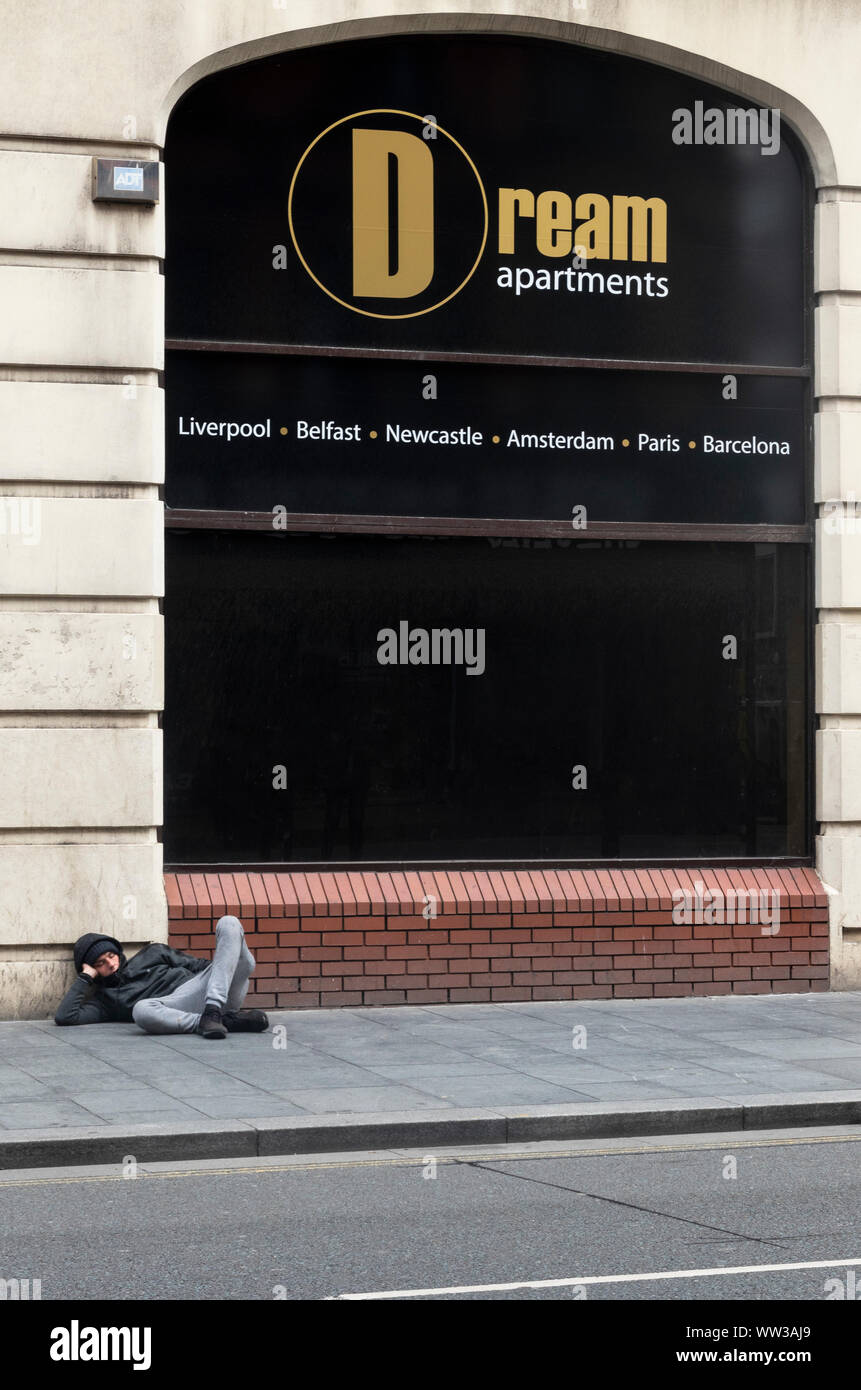 Ironisches Bild eines jungen Mannes schlafen auf der Straße vor ein Zeichen für Dream Apartments in Liverpool Stockfoto