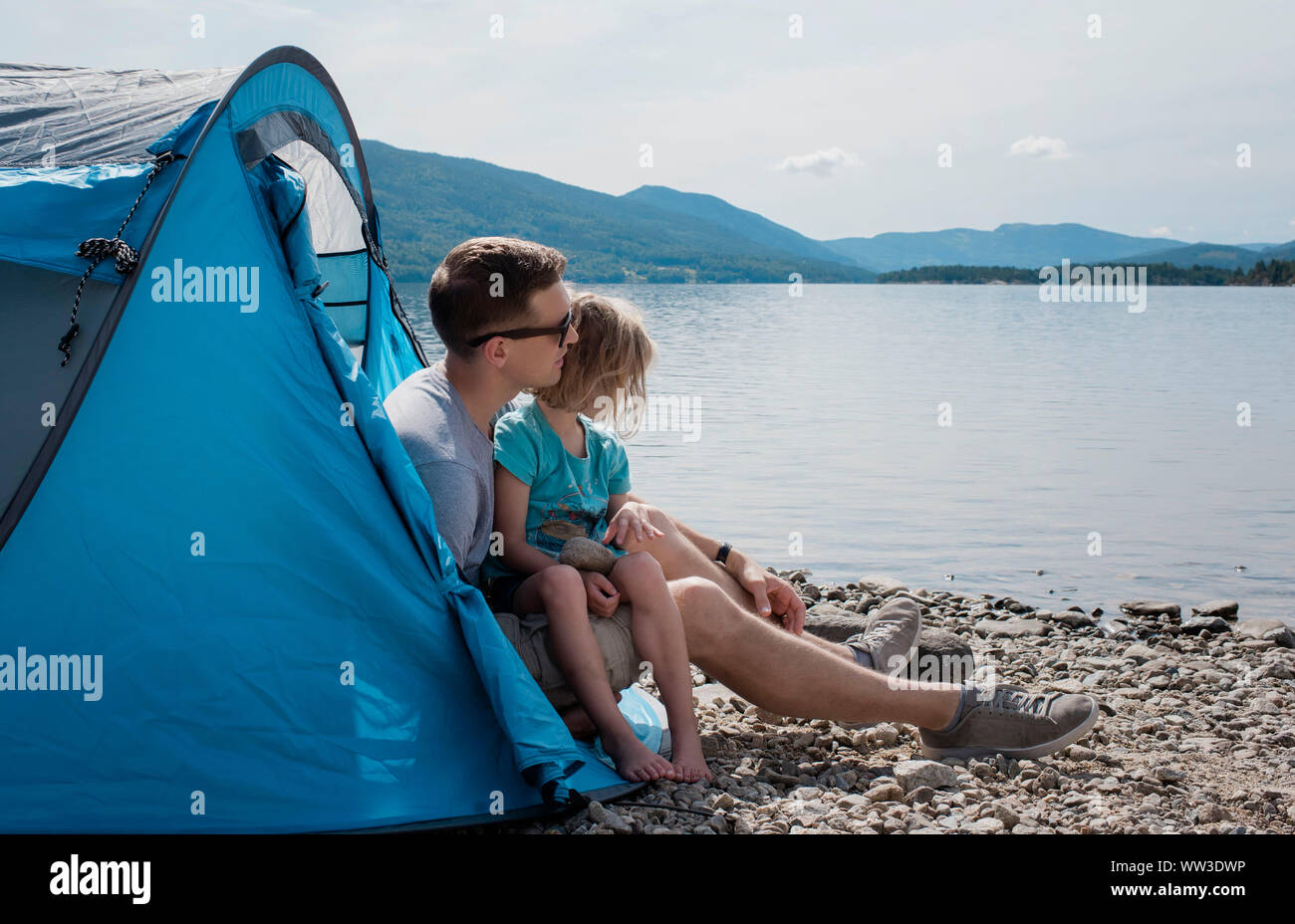 Papa umarmte seine Tochter während des Sitzens in einem Zelt Camping am Meer Stockfoto