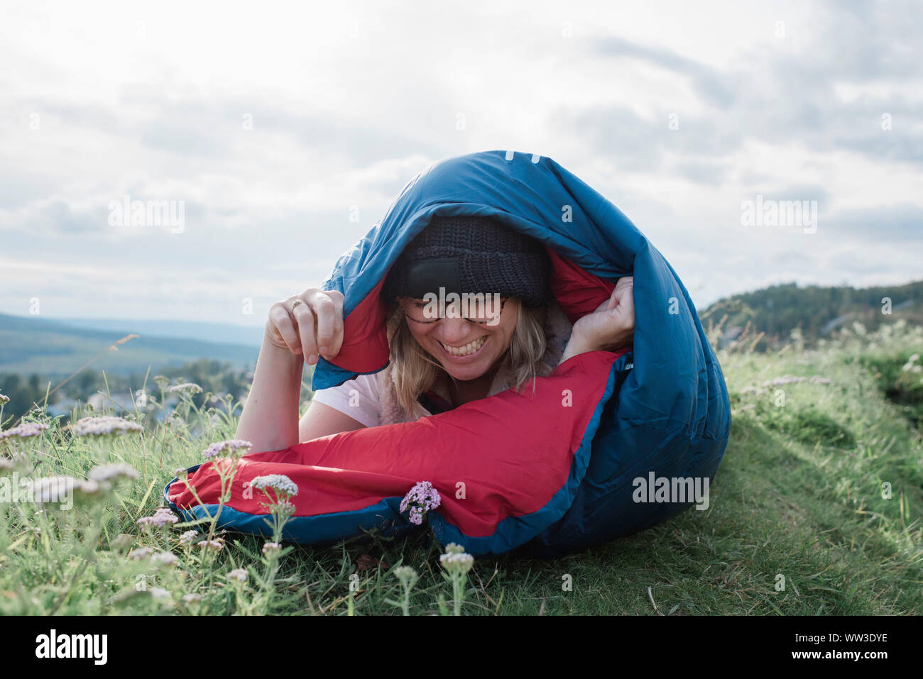 Porträt einer Frau, die in einem Schlafsack beim Camping auf dem Hügel lachen Stockfoto