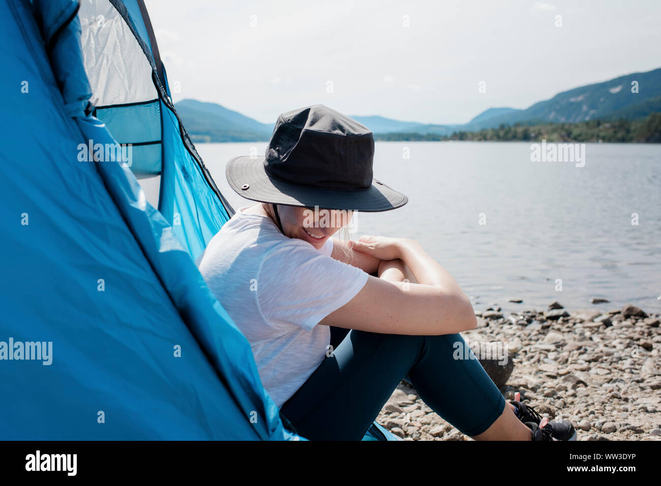 Frau sitzt in einem Zelt lächelnd mit Sonnenhut auf beim Camping Stockfoto