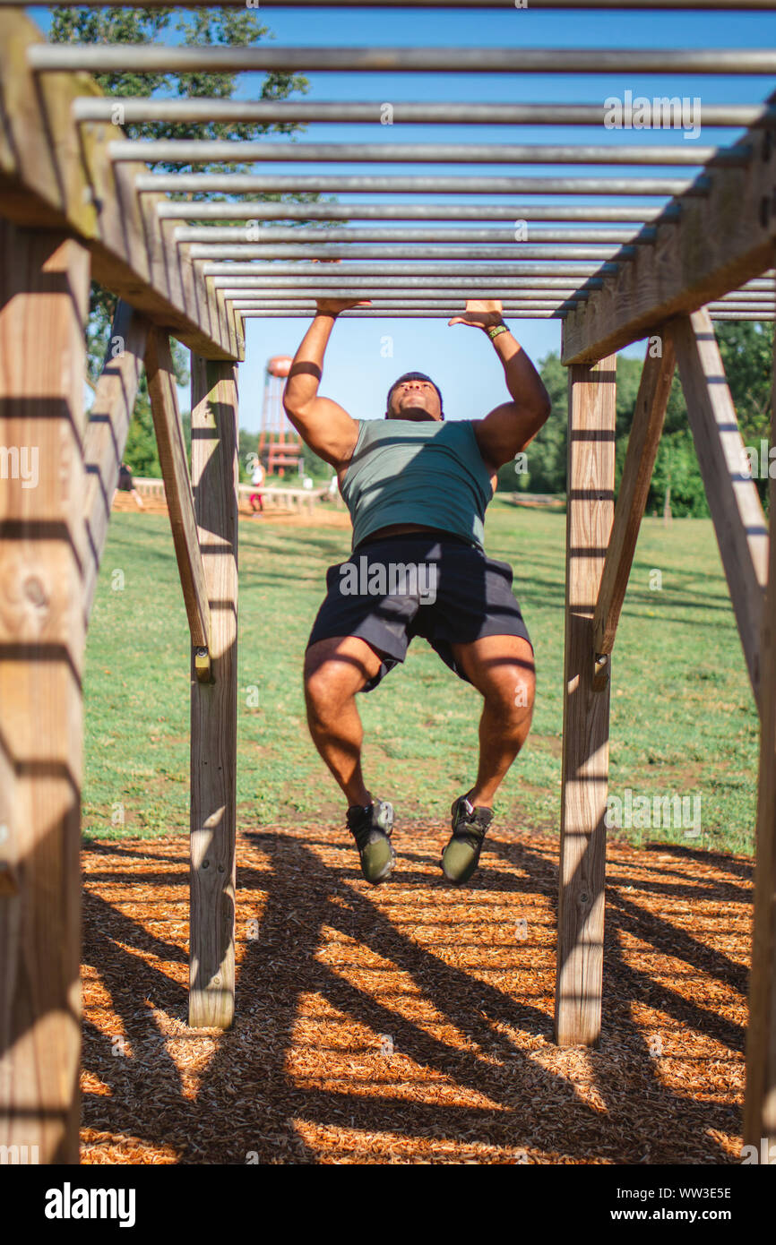 Vorderansicht eines starken Mannes Schwingen über Monkey Bars in Park Stockfoto