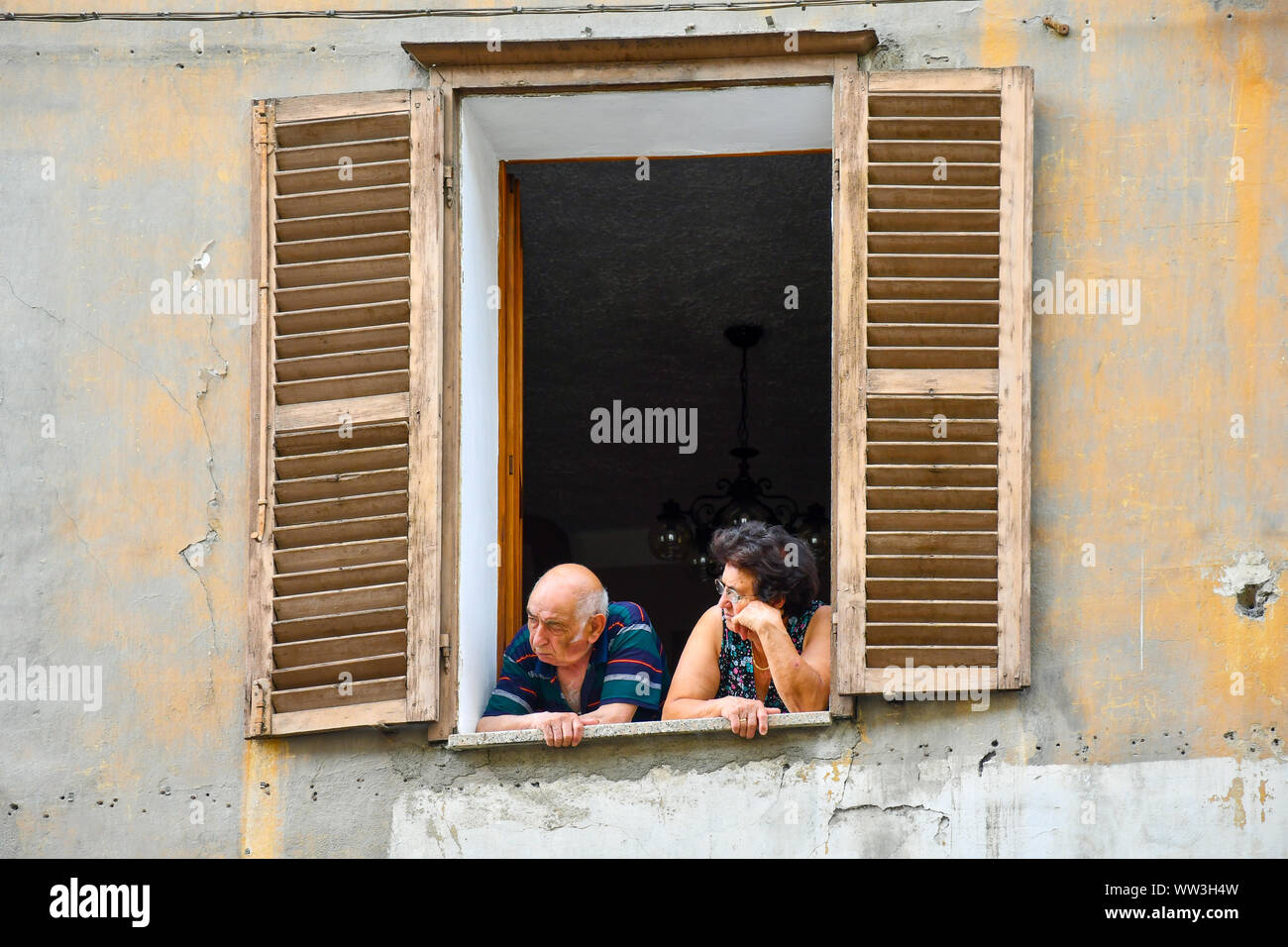 Ein älteres Ehepaar aus dem Fenster Ihrer Wohnung im Zentrum der Stadt Aosta an einem sonnigen Sommertag, Aostatal, Italien Stockfoto