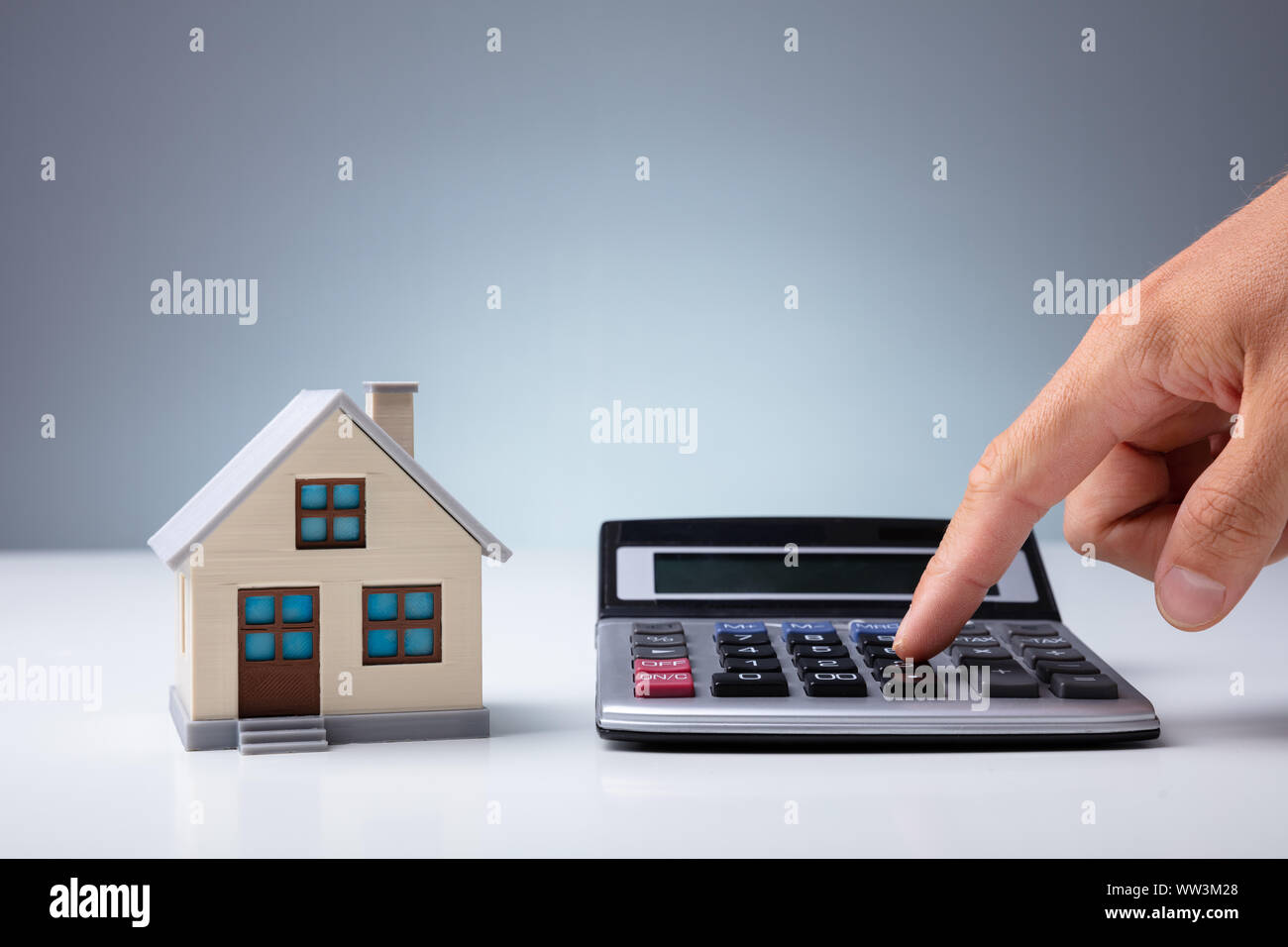 Person's Hand Rechnen mit Taschenrechner in der Nähe von House Modell auf dem Schreibtisch Stockfoto