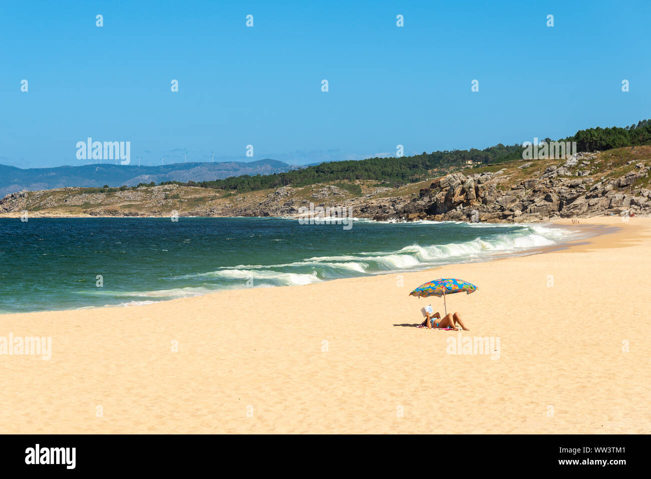 Frau liest ein Buch an einem einsamen Strand in Galicien, Spanien Stockfoto