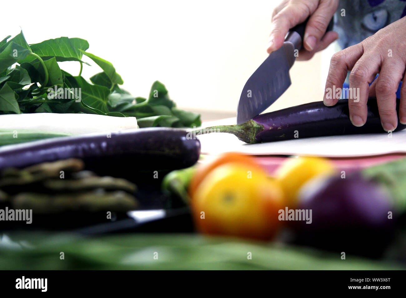 Foto einer Hand schneiden eine Aubergine auf einem Küchentisch mit Gemüse Stockfoto