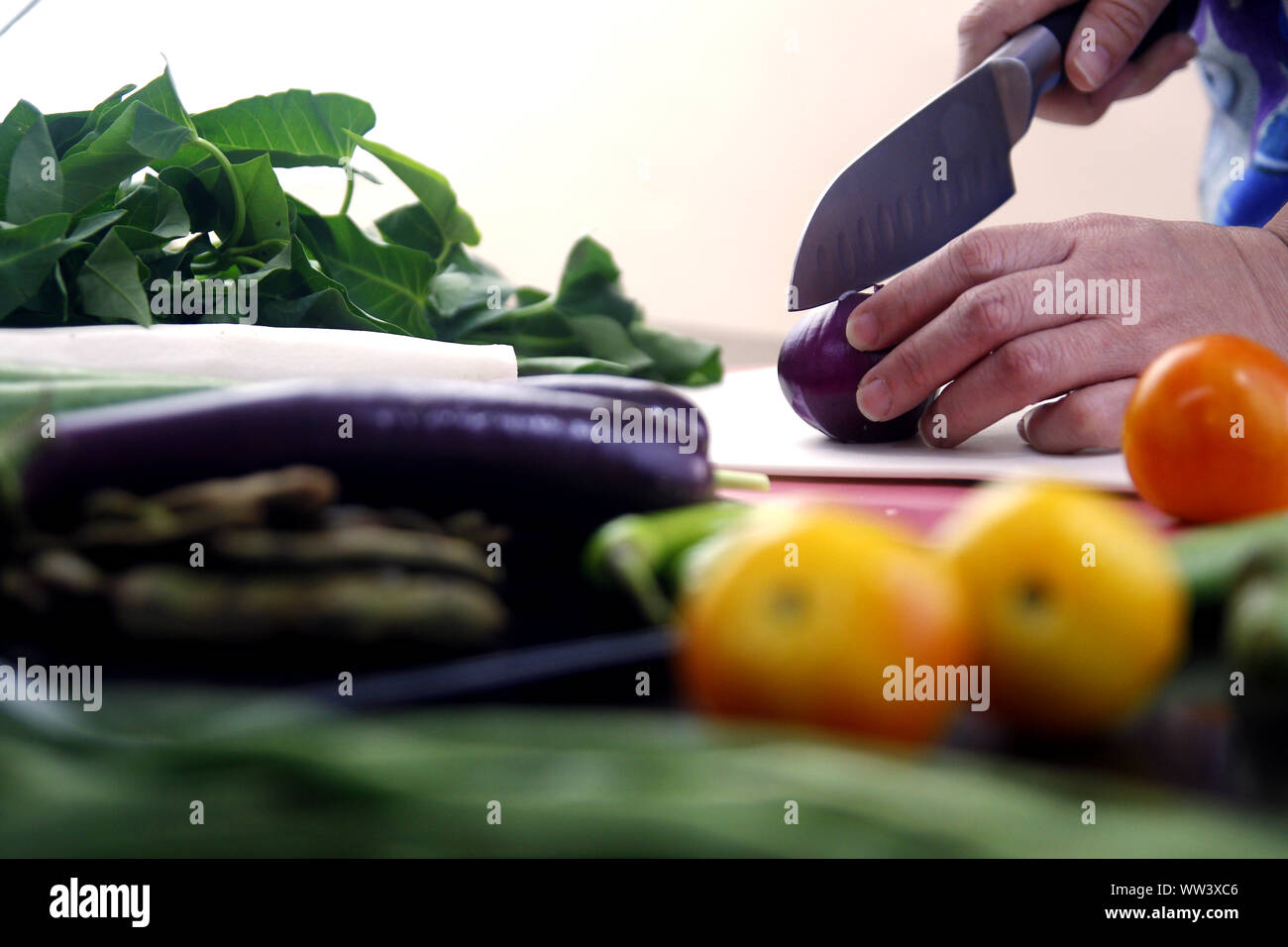 Foto einer Hand schneiden einer Zwiebel auf einem Küchentisch mit Gemüse Stockfoto