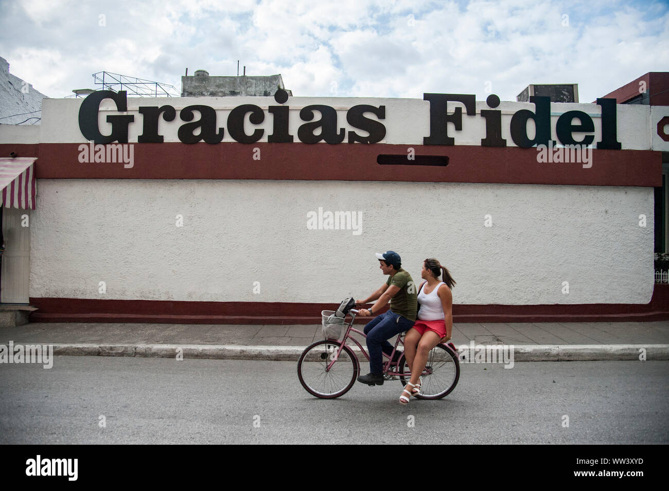 Ein Paar fährt mit dem Fahrrad durch die Straßen von Havanna, Kuba, mit einem Schild zu Ehren des verstorbenen Fidel Castro Stockfoto