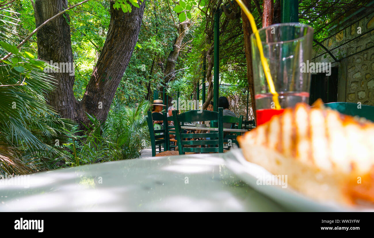 Athen Griechenland - 15. Juli 2019; die Menschen sitzen in kühlen im Schatten der Bäume im Außenbereich der Cafe mit Essen und Trinken in selektiven Fokus forgro Stockfoto