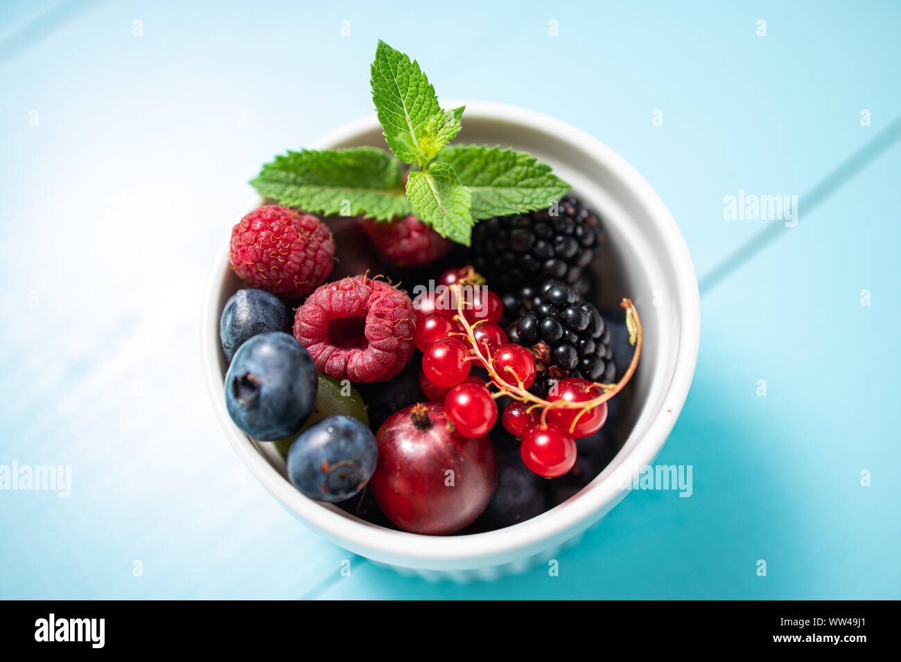 Wild Berry frische Früchte mit minzeblatt in einer Schale auf Holz vintage blauen Hintergrund. Stockfoto