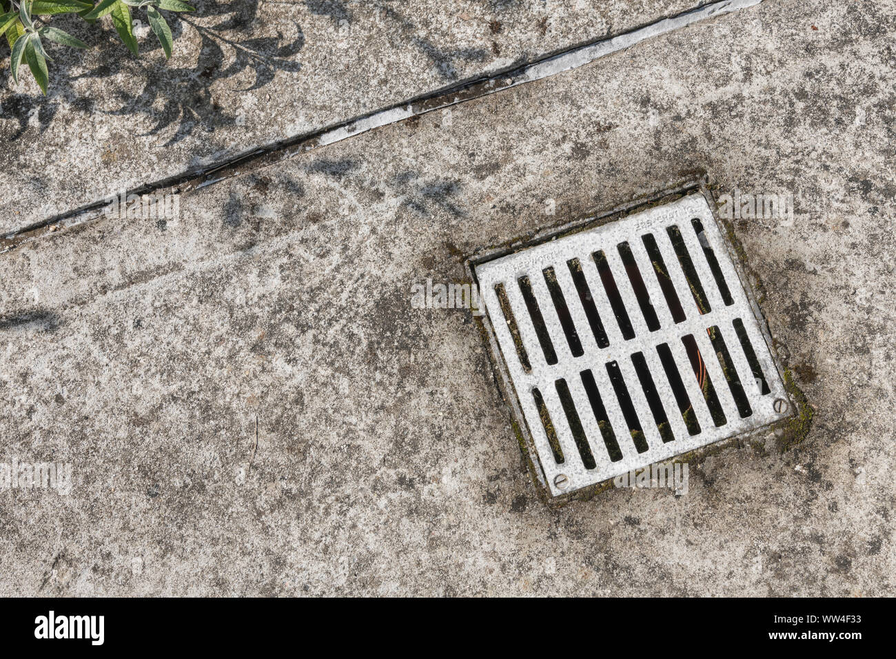 Metall Kanaldeckel (Name des Herstellers geprägte schwach) in einem industriellen Betonplatte. Geld Metapher, oder industrielle Entwässerung. Stockfoto