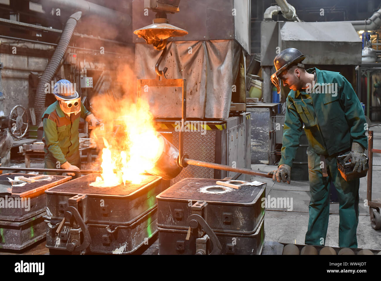 Arbeitnehmer in einer Gießerei gießen ein Werkstück aus Metall - Sicherheit bei der Arbeit und Teamarbeit Stockfoto