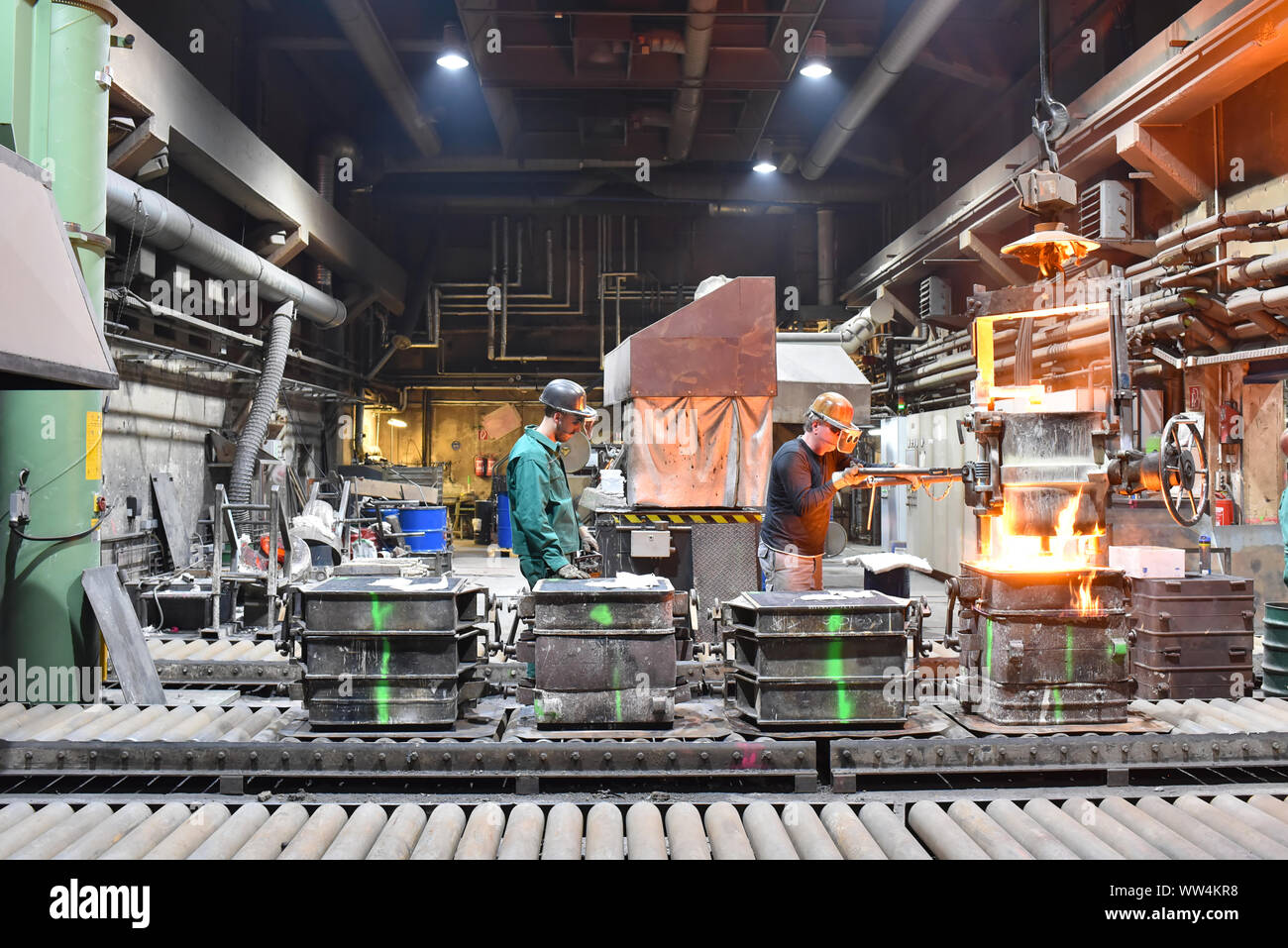 Arbeitnehmer in einer Gießerei gießen ein Werkstück aus Metall - Sicherheit bei der Arbeit und Teamarbeit Stockfoto